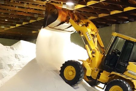 Skid loader pouring rock salt onto bulk pile in bulk rock salt supplier distribution warehouse